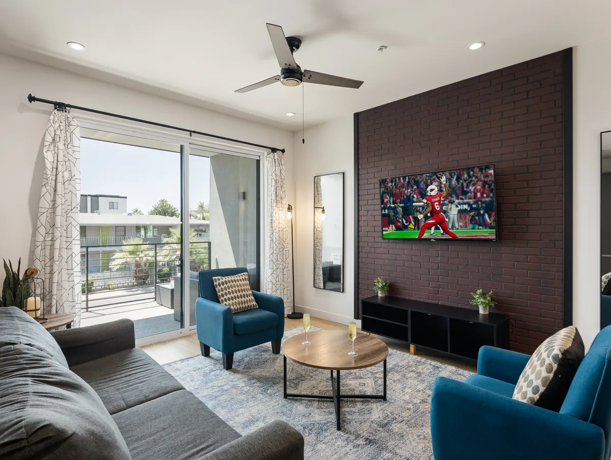 The image showcases a spacious, stylish living area with a plush sofa, vibrant blue chairs, and a large TV as the centerpiece. The coffee table invites guests to gather for drinks or snacks, while the arrangement suggests a perfect setting for watching a game, socializing, or simply relaxing after a day in Old Town Scottsdale.