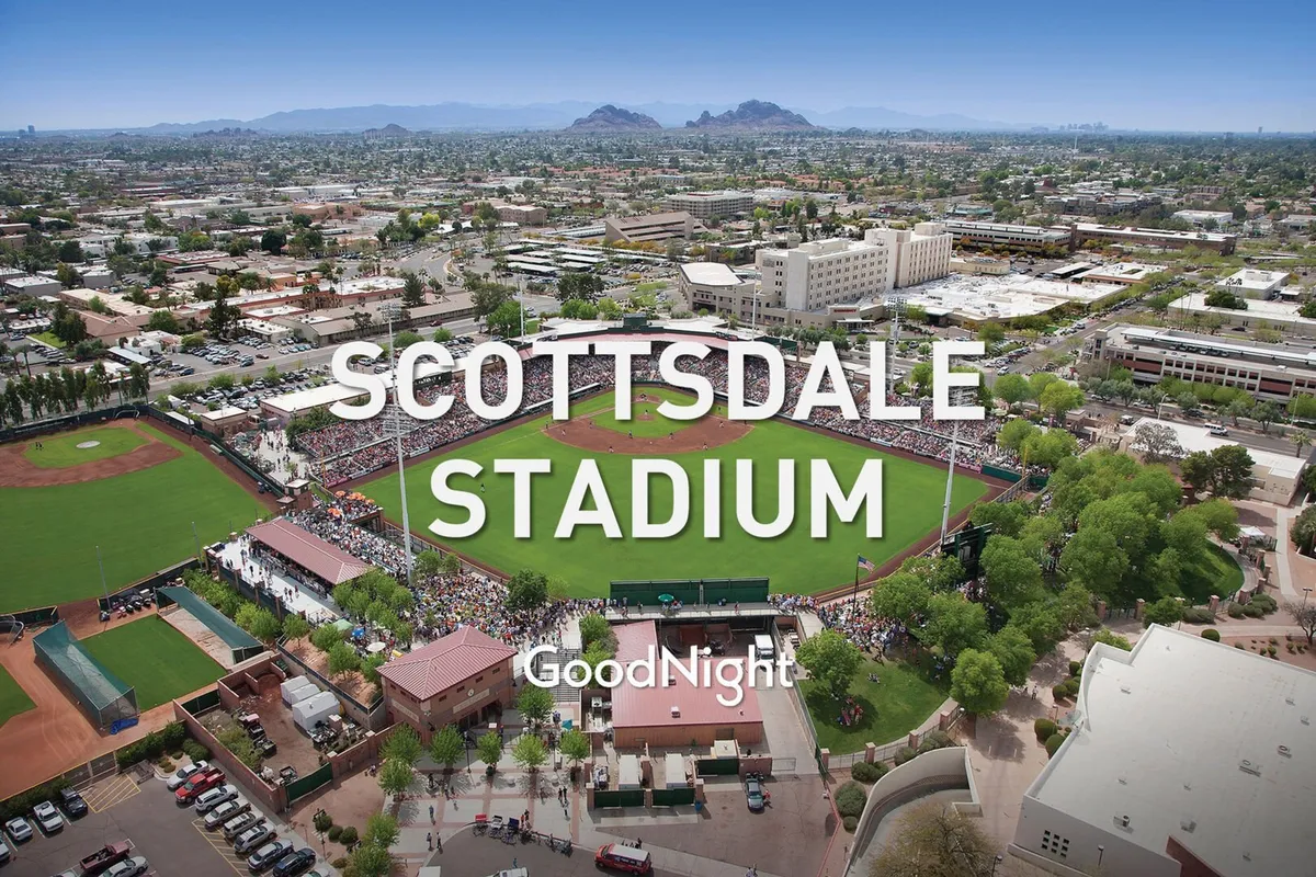 A wide exterior shot of the iconic Scottsdale Stadium with its baseball field, spectator seating, and the surrounding landscape. The stadium is bustling with activity, suggesting local sports events and community gatherings.