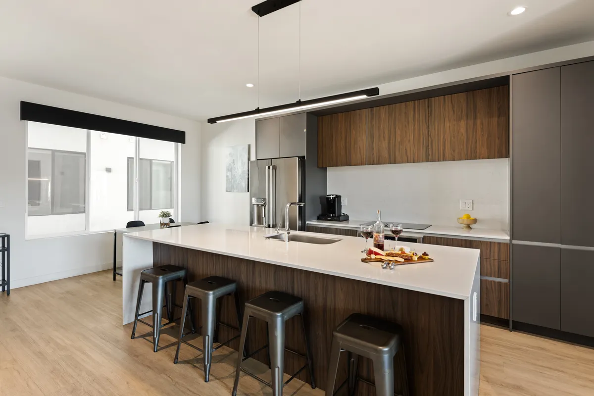 A modern kitchen featuring a large island with stainless steel appliances and wood cabinetry. The kitchen island is topped with a decorative plate of snacks, and the space is brightened by natural light.