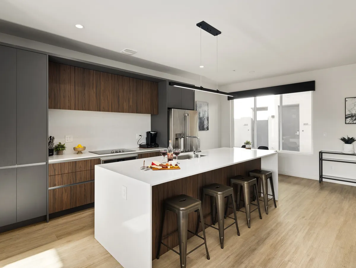 A stylish kitchen interior viewed from the island, with bar stools lined up for casual seating. The countertop features drinks and a fruit platter, suggesting celebration or casual entertaining. Modern glassware and a cheerful vibe add to the sense of group enjoyment.