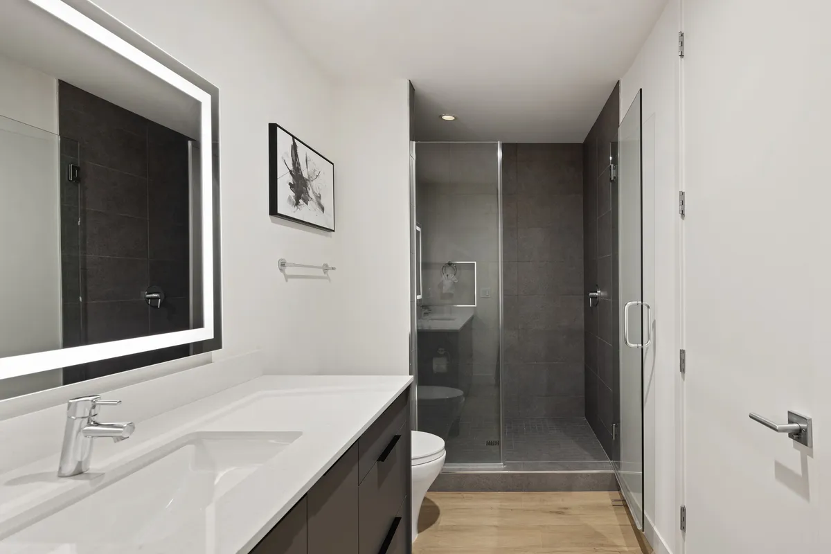 A modern and inviting ensuite bathroom featuring a stylish backlit mirror, glass-enclosed shower, and sleek fixtures. The minimalist design creates a spa-like feel, perfect for personal care routines and relaxation.