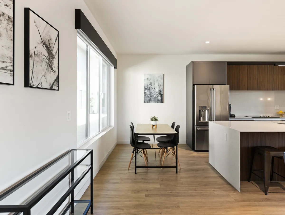 A bright, open-concept interior space featuring a dining table and a spacious kitchen island. The kitchen and dining areas flow together, decorated with modern art and set for a lively meal. The setting is inviting for social gatherings, group meals, and casual conversations.
