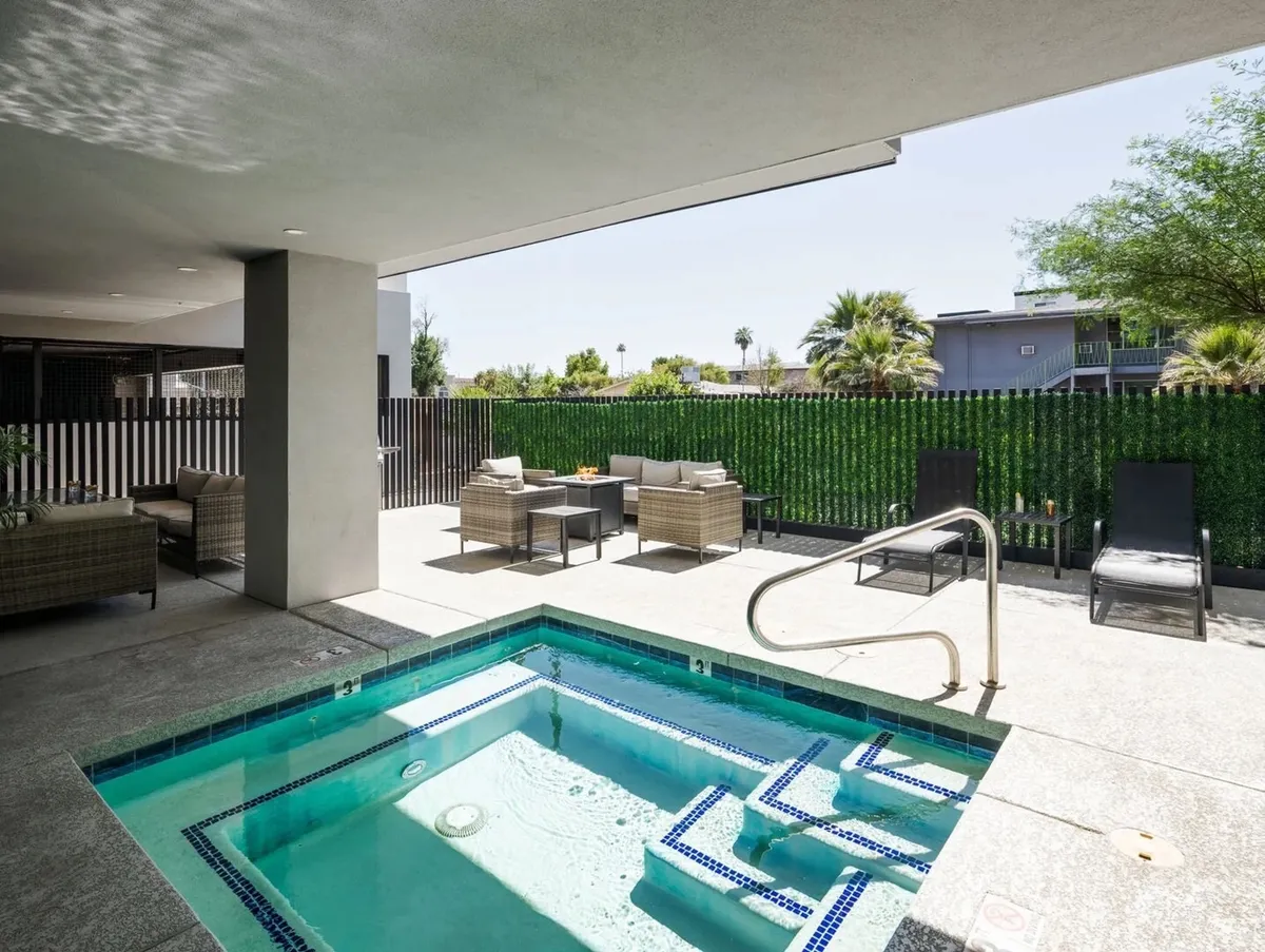 An inviting view of the outdoor spa area, featuring a bubbling hot tub surrounded by comfortable seating and abundant greenery. The setting is tranquil and sunlit, perfect for relaxing soaks by day or night.