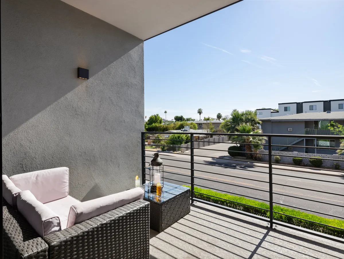 An inviting private balcony with stylish wicker seating and a glass table, offering a relaxed vantage point over the street below. The setup suggests a serene, private retreat perfect for enjoying sunsets, people-watching, or a quiet coffee after a day of exploring.