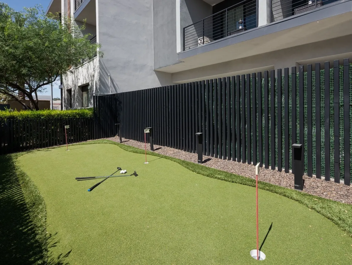 A vibrant putting green set next to modern architecture, complete with golf clubs and shaded seating nearby. The playful, open-air environment encourages friendly competitions and leisurely afternoons.